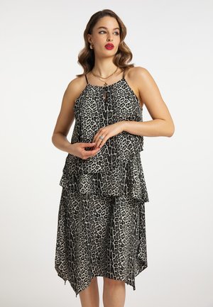 Donna che indossa un vestito senza maniche a strati con stampa leopardata e spalline sottili, abbinato a gioielli dorati e rossetto rosso.