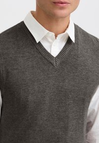 Grauer V-Ausschnitt-Pullover aus Strickstoff mit geripptem Saum und einem weißen Hemd mit Kragen darunter, zeigt eine glatte Textur.