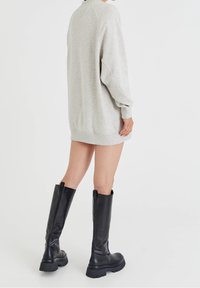 Robe sweat-shirt grise à manches longues avec poignets côtelés, associée à des bottes en cuir noires montantes jusqu'aux genoux avec une semelle épaisse.