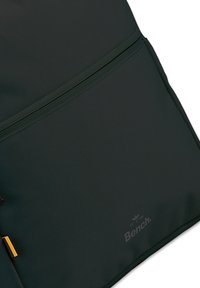 Donkergroene rugzak met een textuur van nylon, voorzien van een voorvak met rits en een subtiele merklogo onderaan.