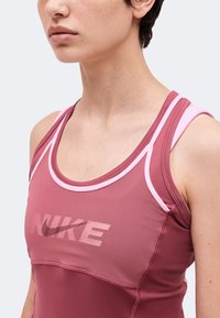 Gros plan d'une personne portant un débardeur de sport rose Nike avec une bordure rose clair et un logo sur la poitrine, montrant la zone du cou et de l'épaule.