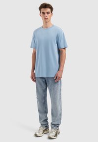 Lichtblauwe t-shirt met korte mouwen, ronde halslijn, gecombineerd met lichtblauwe versleten jeans en metallic sneakers met complexe details.