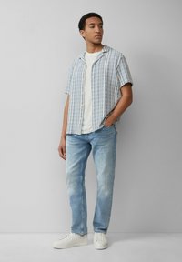 Korte mouwen, overhemd met knopen met blauw en wit verticale strepen, gecombineerd met lichtblauwe jeans en witte sneakers. Gladde textuur.