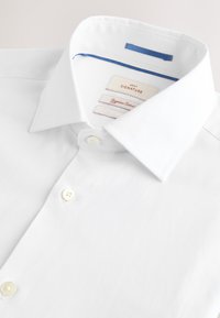 Camicia bianca a maniche corte con bottoni e colletto, caratterizzata da un dettaglio blu all'interno del colletto e tre etichette all'altezza del collo.