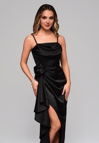 Černé večerní šaty s výstřihem do cowl, přiléhavým korzetem a drapovanou sukní s bočním rozparkem a květinovým detailem v pase.