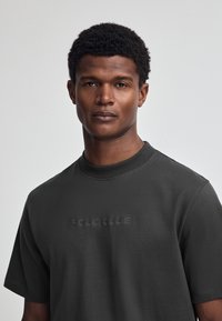 Dunkelgraues T-Shirt aus weichem Stoff mit geripptem Rundhalsausschnitt und prägnantem, erhabenem Schriftzug "POLO CLUB" auf der Vorderseite.