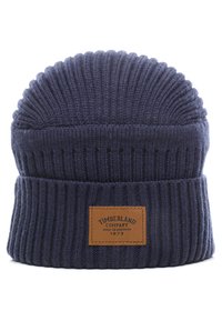 Berretto lavorato a maglia blu scuro con una texture a coste, caratterizzato da una patch in pelle con la scritta "Timberland Company" e un anno, e un design con la parte superiore arrotondata.