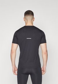 Svart atletisk t-shirt med korta ärmar, slät textur, har ett reflekterande horisontellt tygband på baksidan. Åtsittande design, minimal grafisk profil.