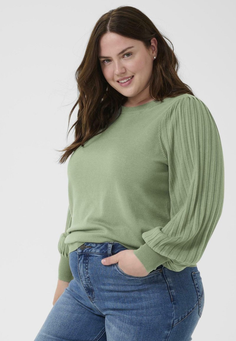 Lys grøn sweater med ribstrikkede pufærmer. Kombineret med blå jeans, der fremhæver en glat tekstur, rund halsudskæring og en tætsiddende pasform.