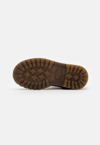 Semelle de botte en caoutchouc brun avec un motif de semelle, présentant des designs hexagonaux et croisés pour une meilleure adhérence, des côtés texturés et des contours bien définis.