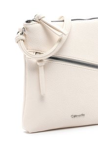Sac bandoulière en cuir beige clair avec surface texturée, fermeture éclair argentée, sangle réglable et petit logo métallique de la marque sur le devant.