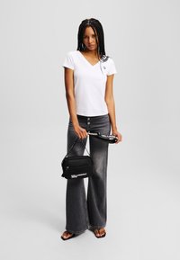 Tricou alb cu mânecă scurtă și decolteu în V, având un logo mic, asortat cu blugi gri evazați cu talie înaltă și o geantă neagră tip crossbody.