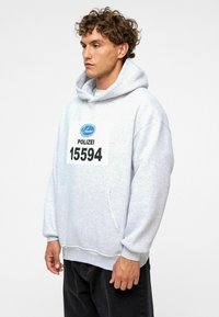 Lichtgrijze hoodie met een voorzak, voorzien van een "POLIZEI" graphic en het nummer 15594. Gemaakt van zachte stof met een relaxte pasvorm.