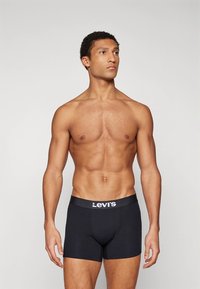 Fekete boxeralsó széles derékpánttal, amelyen Levi's logó található, testhezálló szabással és sima textúrával, semleges testtartású férfi modellen viselve.