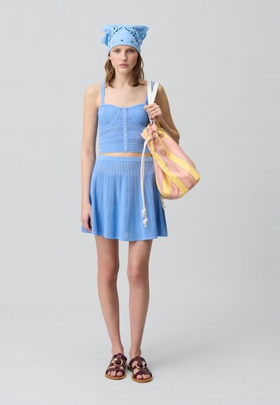 Top corto a coste di colore blu chiaro con bottoni, gonna plissettata coordinata e borsa a tracolla con motivo in rosa e giallo. Sandali marroni con fibbie.
