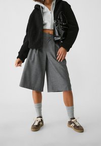 Musta teksturoitu fleece-takki, harmaat ruudulliset culottes-housut, harmaat sukat ja ruskeat lenkkarit valkoisilla nauhoilla. Asusteina pieni musta laukku.