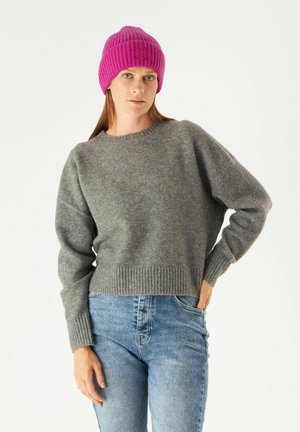 Grijze wollen trui met een ronde hals en een geribbelde zoom, gecombineerd met lichtblauwe jeans. Een felroze geribbelde beanie maakt de outfit compleet.