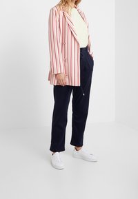 Blazer a rayas en tela rosa y roja, combinado con pantalones navy y zapatillas blancas. El blazer tiene un diseño de doble botonadura y mangas largas.