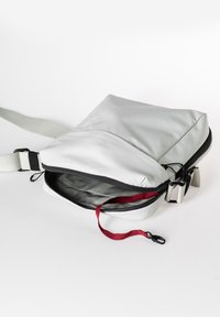 Weiße wasserdichte Tasche mit flachem Design, grauem Innenraum, schwarzem Reißverschluss und verstellbarem Gurt; verfügt über einen roten Reißverschlusszieher für einfachen Zugriff.