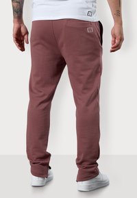 Bordeauxrote Sweatpants mit Slim-Fit, aus Baumwolle. Mit einem kleinen Logo-Detail auf der Rückseite und seitlichen Taschen. Kombiniert mit weißen Sneakers.