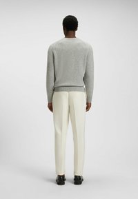 Maglione grigio realizzato in materiale a maglia con colletto rotondo, polsini e orlo a costine. Abbinato a pantaloni bianchi e scarpe nere.
