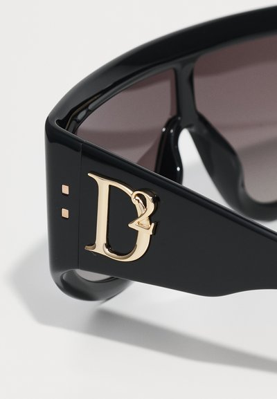 Black oversized sunglasses with gradient lenses, featuring a gold logo accent on the temple, smooth texture, and contemporary design.