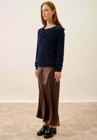 Tummansininen vetoketjullinen huppari, pehmeä materiaali; yhdistetty ruskean satiinisen maksihameen ja mustien korkokenkien kanssa. Yksinkertainen, moderni muotoilu.