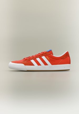 Červená teniska Adidas s bílými pruhy, bílou podrážkou, modrým detailem na jazyku a zlatým nápisem "NORA" na boku.