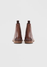 Botas Chelsea de couro castanho com painéis elásticos laterais, bico arredondado e sola de borracha. Textura suave com um salto baixo e laço na parte de trás.