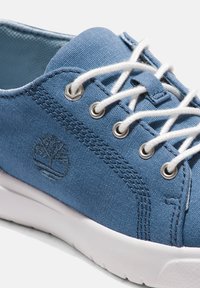 Blaue Canvas-Sneaker mit weißen Ösen, runden Schnürsenkeln und einem strukturierten Seitenlogo. Die Sohle ist weiß und hat ein leicht erhöhtes Design.
