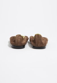 Zapatos de ante marrón sin cordones con forma redondeada, que presentan un detalle de acento amarillo a lo largo del borde y una suela de goma negra.