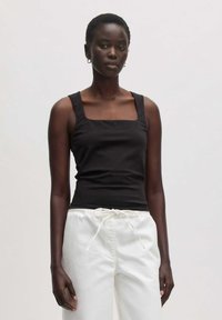 Schwarzes Top mit quadratischem Ausschnitt aus Baumwolle, kombiniert mit weißen Tuchhosen mit Kordelzug. Verfügt über breite Träger und eine taillierte Silhouette.