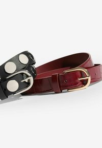 Két öv: az egyik fekete bőr, ezüst tüskékkel és ezüst csattal, a másik mélyvörös fényes öv arany csattal és finom részletekkel.