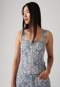 Top de denim azul com padrão floral, decote quadrado, fecho frontal e alças largas. Tecido texturizado e design ajustado com um bolso.