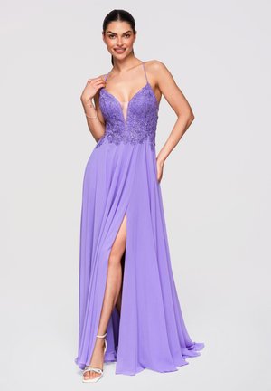 Mujer con vestido lila sin mangas con corsé de encaje, abertura hasta el muslo y tirantes finos, posando con una mano en la cadera y la otra tocando su hombro.