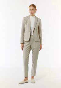 Jasnoszara, dopasowana marynarka z pojedynczym guzikiem, w zestawie z dopasowanymi spodniami i białym topem z wysokim kołnierzem. Gładki materiał, minimalistyczny design.