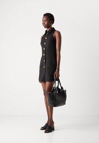 Črna brezrokavna obleka z zlatimi gumbi, v kombinaciji s črno torbico in črnimi sandalmi. Gladka tkanina z prilagojenim krojem.