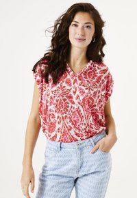 Top de manga corta rojo y blanco con estampado, con escote en V, combinado con jeans de textura azul claro. Diseño sencillo, ajuste casual.