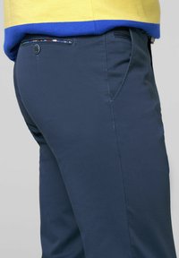 Marineblaue Hose aus strukturiertem Stoff, mit einer Gesäßtasche mit Knopf und mehrfarbigem Futter. Seitennähte sichtbar.
