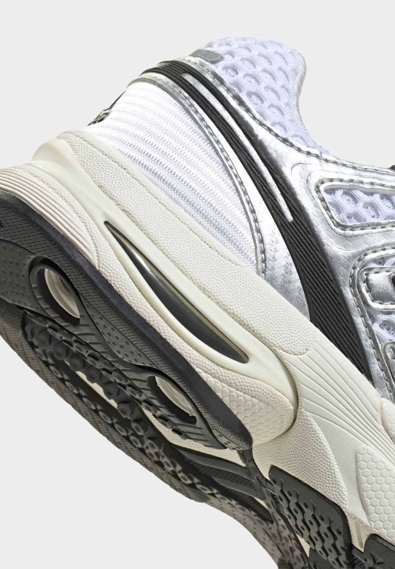 Chaussure de sport blanche et argentée montrant une semelle extérieure texturée, une semelle intermédiaire rembourrée et une tige en mesh respirant avec des détails noirs.