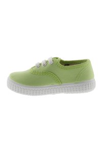 Zapatilla de lona verde claro con suela de goma blanca, tres ojales blancos y costuras en contraste a lo largo del costado. Diseño de caña baja, textura mínima.