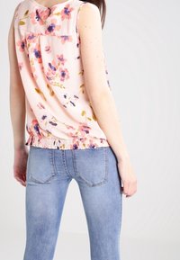 Květinový bezramínkový top ve světle růžové barvě s barevnými květinami a nařaseným lemem, doplněný o úzké světle modré džíny s zadními kapsami.