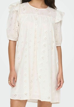 Robe blanche en broderie anglaise avec manches courtes bouffantes, encolure ronde et motifs floraux. Elle présente une coupe ample et des détails subtils en volants.