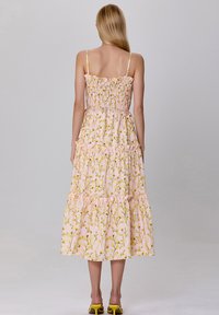 Robe midi florale rose avec un corsage smocké, des niveaux froncés et des bretelles fines. Arbore un motif floral jaune sur un fond pastel.
