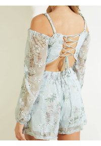 Mono de color azul claro con bordados florales, mangas largas de tejido transparente y un detalle de cierre con cordones en la parte posterior. Cintura elástica y dobladillo con forma de ondas.