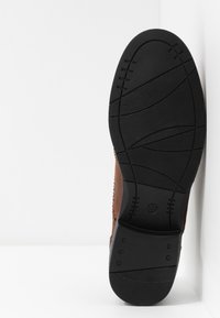 Chaussure en cuir marron avec une tige texturée et une semelle en caoutchouc noire présentant des rainures flexibles et une indication de taille 37.