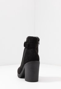 Černá semišová kotníková bota s robustním podpatkem, vybavená bočním zipem a elastickými panely. Podpatek má strukturovaný, rýhovaný povrch.