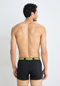 Boxeri negri cu un brâu neon galben "PUMA", confecționați dintr-un material neted și elastic, arătați din spate pe o persoană.