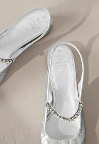 Valkoiset slingback-kengät, joissa on sileä nahkapinta ja koristeellinen strassivyö jalkapöydän yli.