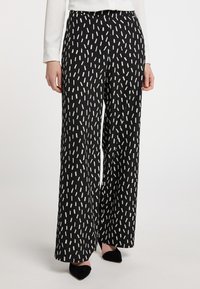 Schwarze weite Hosen mit weißem abstraktem Muster. Verfügt über eine glatte Stofftextur und eine lockere Passform, Teil eines modernen Designs.